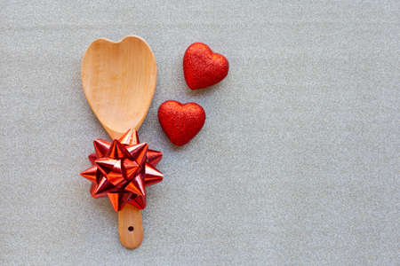 The red heart shapes and wooden spoon with red bow on silver glitter paper background in love concept for valentines day.の写真素材