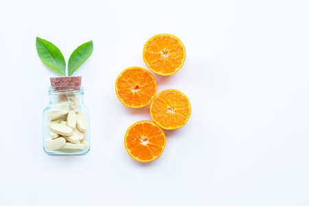 Vitamin C bottle and pills with orange fruit on white background. Copy spaceの写真素材