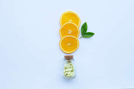 Vitamin C bottle and pills with orange fruit slices on white background.の写真素材
