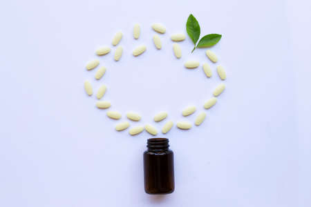 Vitamin C bottle and pills with green leavs on white. background.