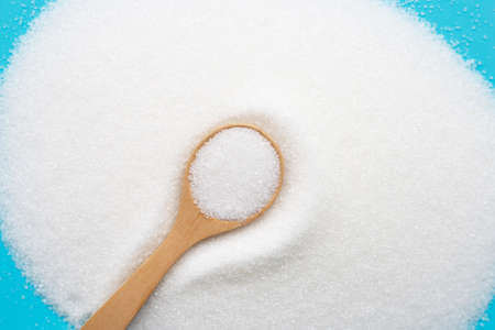 Wooden spoon with white granulated sugar on blue background. Top view