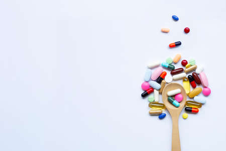 Colorful tablets, capsules and pills with wooden spoon on white background.