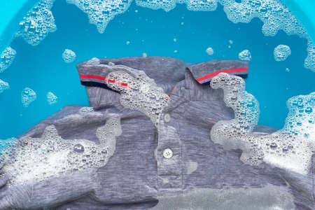 Grey polo shirt soak in powder detergent water dissolution, washing cloth. Laundry concept