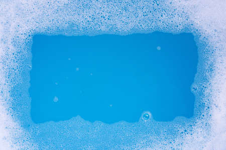 Frame made of detergent foam bubble. Blue background. Top view