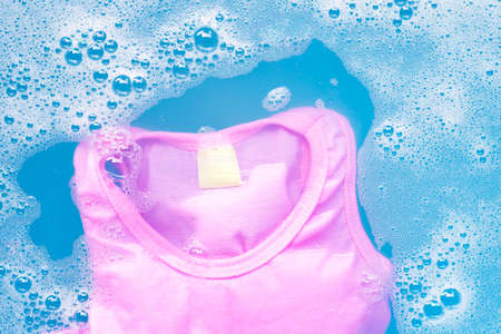 Pink kid sleeveless shirt soak in baby laundry detergent water dissolution, washing cloth, blue background, Laundry concept.の写真素材