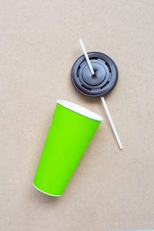 Green paper coffee cup with straw and plastic cap on plywood background.