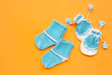 Baby gloves and socks on orange background. Top view