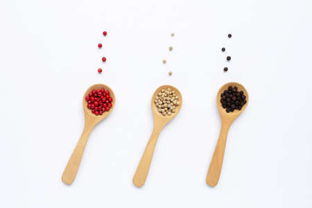 Red, white and black peppercorns with wooden spoon on white background.の写真素材