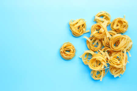 Uncooked Italian pasta tagliatelle nest on blue background. Copy space