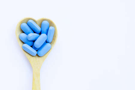Medical blue pills with heart shaped wooden spoon on white background. Copy spaceの写真素材