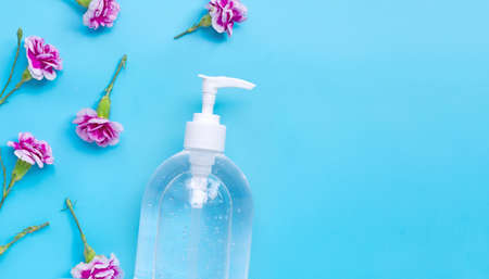 Alcohol hand sanitizer gel in pump bottle with carnation flower on blue background. Copy space