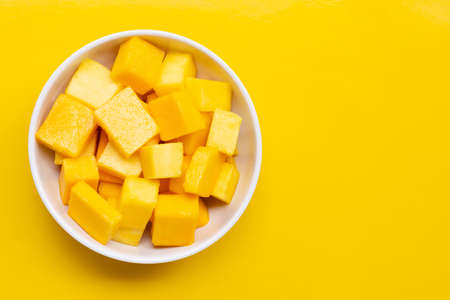 Tropical fruit, Mango cube slices in white bowl on yellow background. Copy space