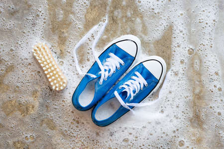 Sneakers with foam of powder detergent water dissolution and wooden brush on cement floor. Washing...