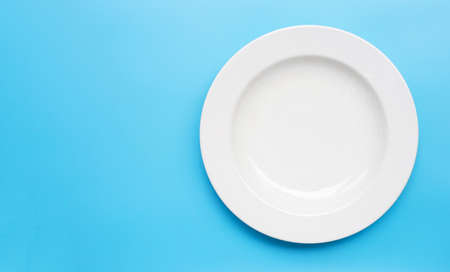 Empty white ceramic plate on blue background. Copy spaceの写真素材