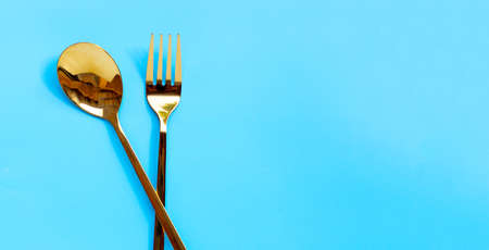 Golden spoon and fork on blue background.  Copy spaceの写真素材