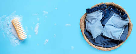 Jeans in laundry basket with wooden brush for cleaning clothes on foam of powder detergent water dissolution on blue background. Top viewの写真素材