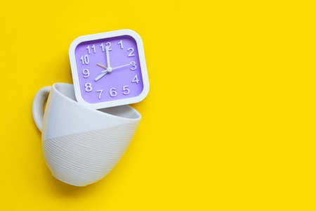 Clock in coffee cup on yellow background. Copy spaceの写真素材