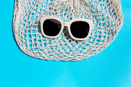 Sunglasses with mesh bag on blue background. Enjoy holiday concept. Copy spaceの写真素材