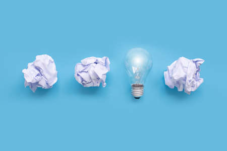 Light bulb  with white crumpled paper ball on blue background. Top view