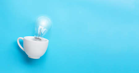Light bulb in white cup on blue background. Ideas and creative thinking concept. Copy spaceの写真素材