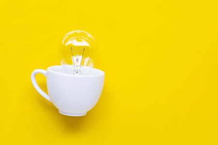  Light bulb in white cup on yellow background. Ideas and creative thinking concept. Copy space