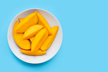 Tropical fruit, Mango slices on white dish on blue background. Copy spaceの写真素材
