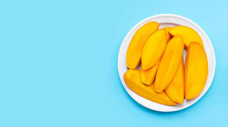 Tropical fruit, Mango slices on white dish on blue background. Copy spaceの写真素材
