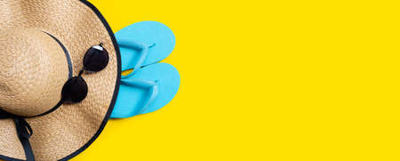 Summer hat with sunglasses and blue flip flops on yellow background. Enjoy holiday concept. Copy spaceの写真素材