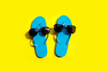 Blue flip flops with sunglasses on yellow background. Enjoy summer holiday concept. Copy spaceの写真素材