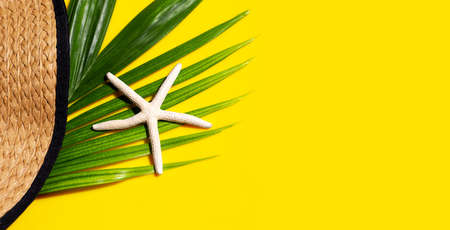 Summer hat with starfish on tropical palm leaves with  on yellow background. Top view