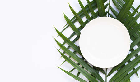 Empty white ceramic plate on tropical palm leaves on white background. Top viewの写真素材