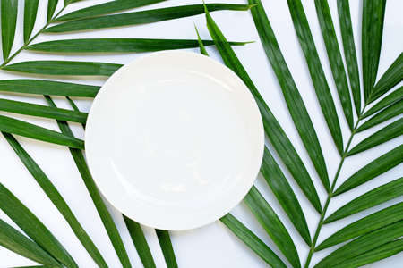 Empty white ceramic plate on tropical palm leaves on white background. Top viewの写真素材
