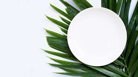 Empty white ceramic plate on tropical palm leaves on white background. Top viewの写真素材