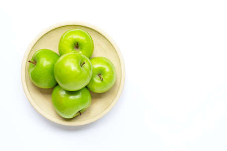 Fresh green apples on pottery plate on white background. Copy space
