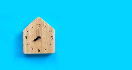 Miniature house wooden clock on blue background. Copy space