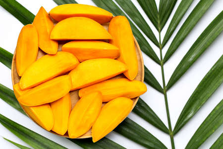 Mango slices on wooden plate on tropical palm leaves. Top viewの写真素材