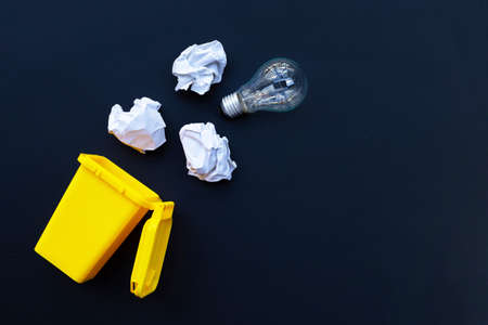 Yellow bin with light bulb and white crumpled paper on dark background. Ideas and creative thinking...