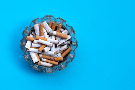 Cigarettes buds in a transparent ashtray on blue