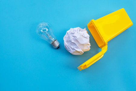 Yellow bin with light bulb and white crumpled paper on blue background. Ideas and creative thinking concept. Top viewの写真素材