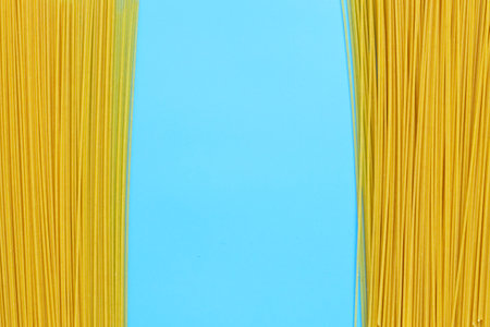 Yellow long spaghetti on blue background. Copy spaceの写真素材