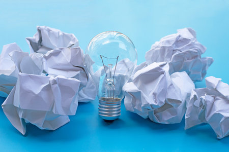 Light bulb with white crumpled paper balls on blue background. Ideas and creative thinking concept.の写真素材