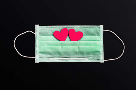 Two pink wooden hearts on protective medical mask on dark background.の写真素材