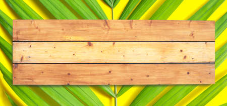 Wooden space on tropical palm leaves on yellow surface. Summer background concept