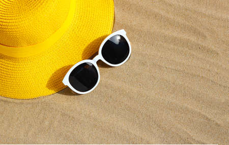Yellow summer hat with sunglasses on sand