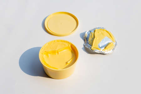 Open round container with butter or margarine on white background.