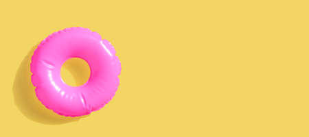 Pink inflatable swimming pool ring on yellow surfaceの写真素材