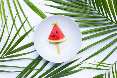 Watermelon slice in white plate on tropical palm leaves