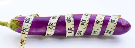 Long purple eggplant wrapped in measuring tape on white background.の写真素材