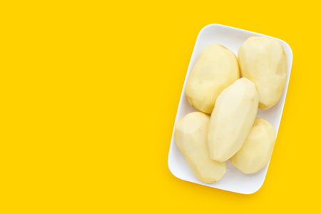 Raw peeled potatoes in white plate on yellow background.の写真素材