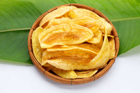 Banana slice chips in bamboo basket on green leaf and white background.の写真素材